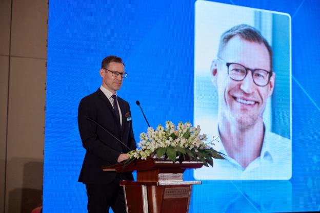 A person standing at a podium with microphones and flowers

Description automatically generated with medium confidence