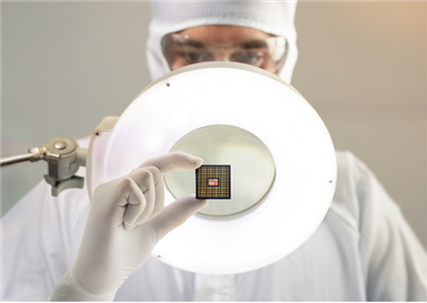 A person in protective gear looking at a microchip
Description automatically generated